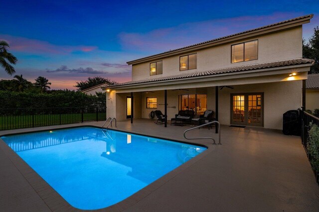 pool at dusk with a patio, french doors, outdoor lounge area, and ceiling fan