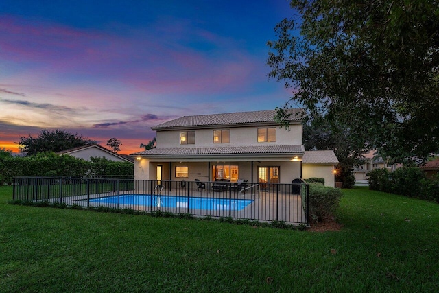 back house at dusk featuring a patio, a fenced in pool, and a lawn