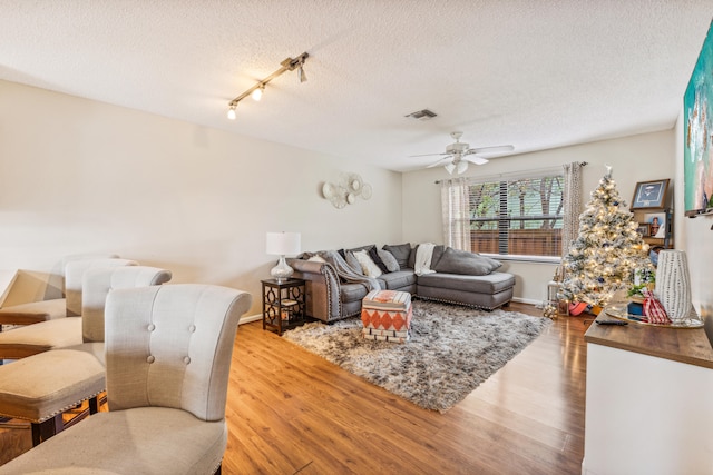 living room featuring ceiling fan, hardwood / wood-style flooring, and a textured ceiling