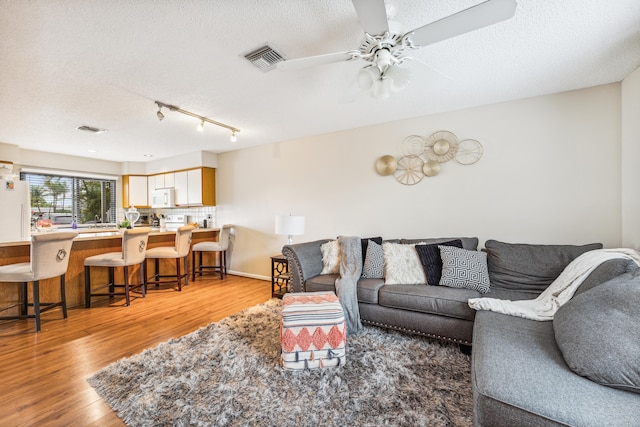 living room featuring ceiling fan, light hardwood / wood-style flooring, and a textured ceiling