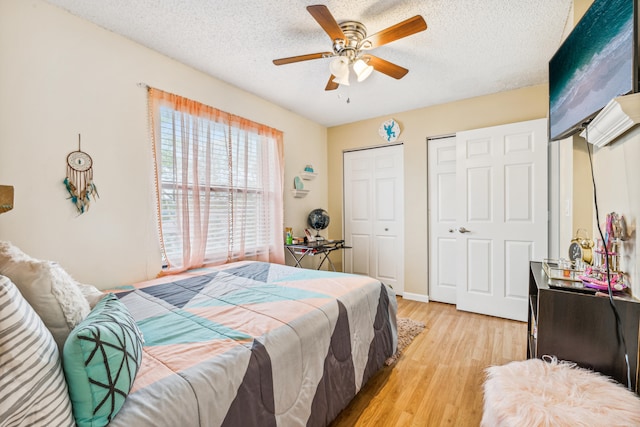 bedroom featuring ceiling fan, two closets, light hardwood / wood-style floors, and a textured ceiling