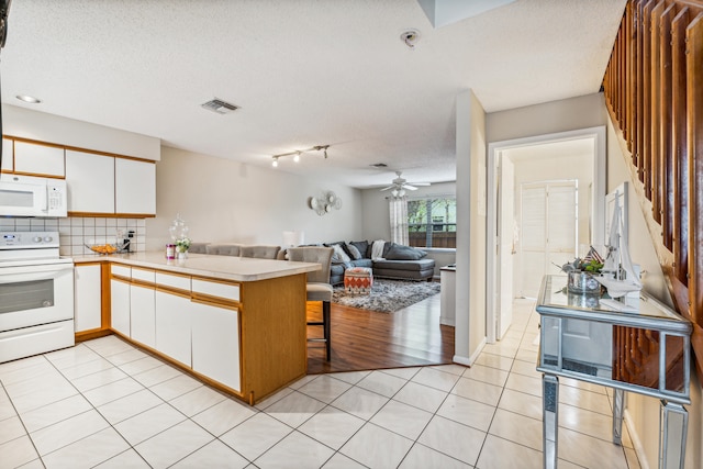 kitchen with white appliances, kitchen peninsula, white cabinetry, light tile patterned floors, and a textured ceiling