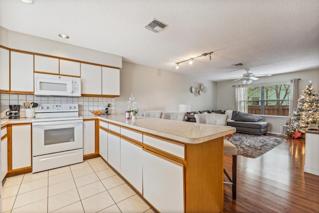 kitchen with white appliances, light hardwood / wood-style floors, kitchen peninsula, white cabinetry, and a breakfast bar area