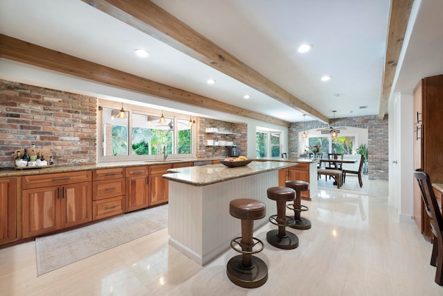 kitchen featuring light stone countertops, beam ceiling, a center island, and a breakfast bar