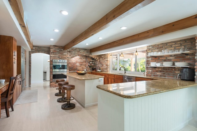 kitchen with beamed ceiling, brick wall, kitchen peninsula, appliances with stainless steel finishes, and a kitchen bar