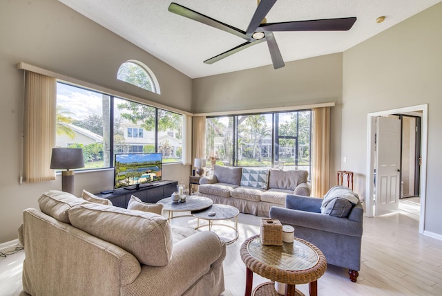 living room featuring high vaulted ceiling, ceiling fan, light wood-type flooring, and a wealth of natural light