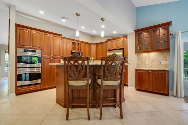 kitchen featuring tasteful backsplash, a kitchen island, decorative light fixtures, stainless steel appliances, and light stone countertops