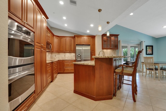 kitchen with lofted ceiling, light stone countertops, a center island, light tile patterned flooring, and appliances with stainless steel finishes