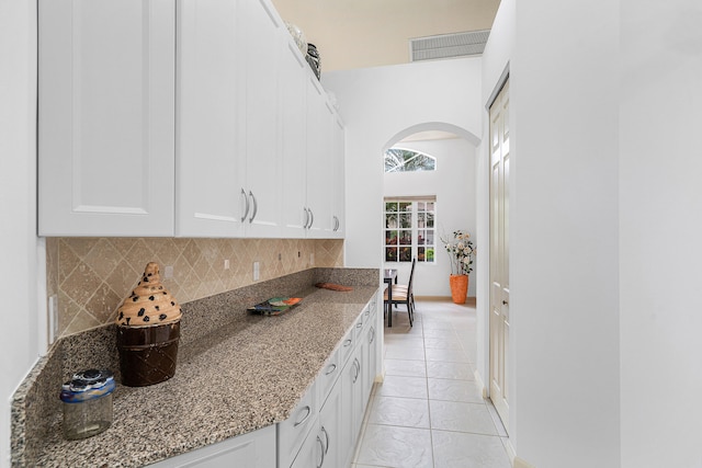 kitchen featuring dark stone countertops, light tile patterned floors, decorative backsplash, and white cabinetry