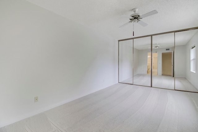 unfurnished bedroom with ceiling fan, a textured ceiling, a closet, and light carpet