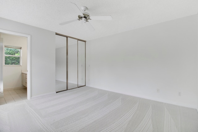 unfurnished bedroom featuring ceiling fan, connected bathroom, a textured ceiling, a closet, and light colored carpet