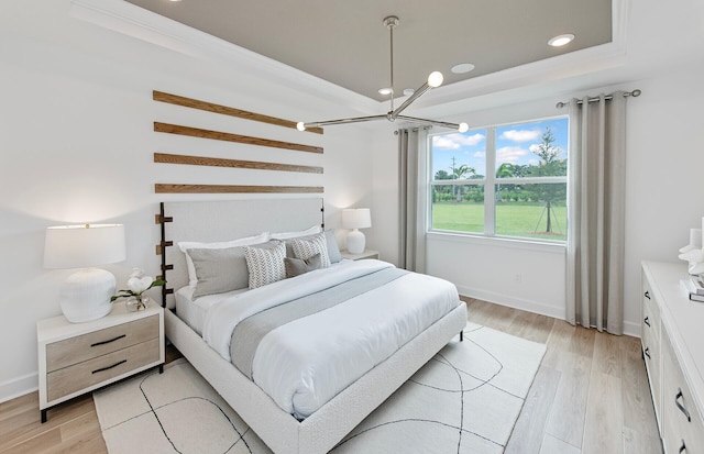 bedroom with an inviting chandelier, light wood finished floors, baseboards, and a tray ceiling