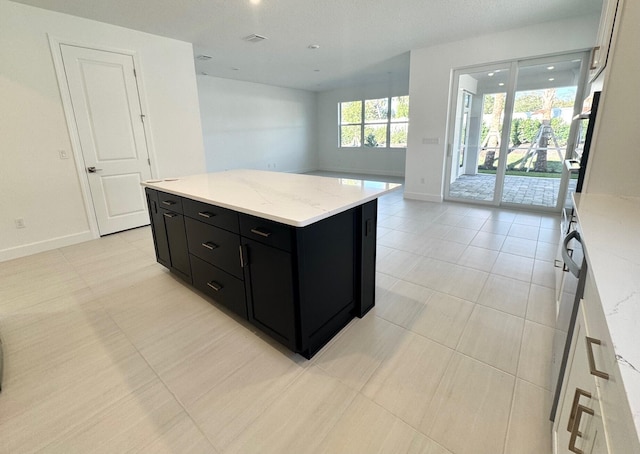 kitchen featuring light stone counters, a kitchen island, baseboards, and dark cabinets