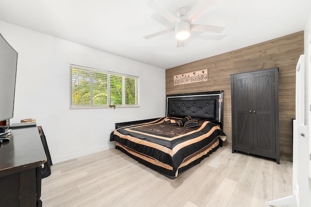 bedroom with ceiling fan, wood walls, and light hardwood / wood-style floors