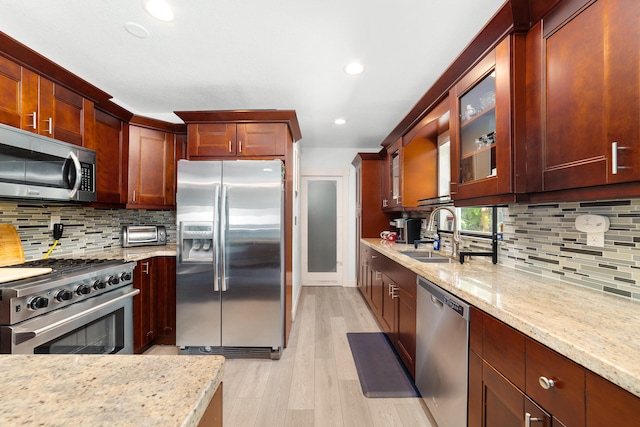 kitchen with light hardwood / wood-style floors, sink, light stone counters, backsplash, and appliances with stainless steel finishes