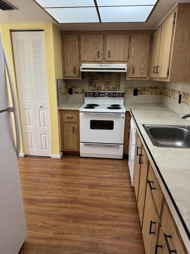 kitchen featuring a skylight, sink, dark hardwood / wood-style floors, backsplash, and white appliances