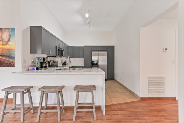 kitchen with gray cabinets, kitchen peninsula, appliances with stainless steel finishes, and light hardwood / wood-style flooring