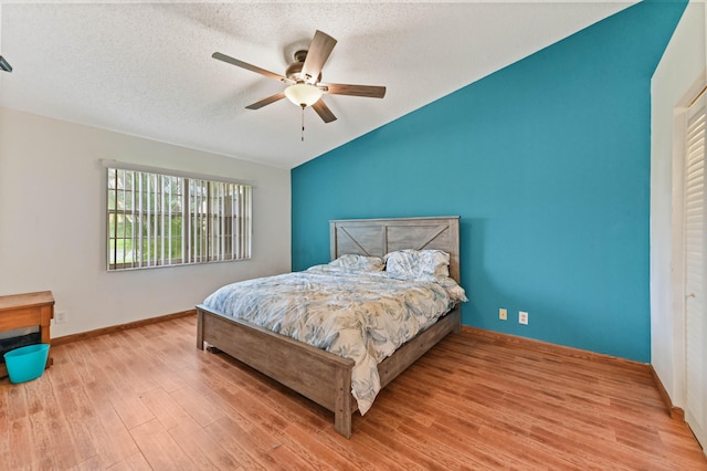 bedroom with a textured ceiling, light wood-type flooring, vaulted ceiling, and ceiling fan