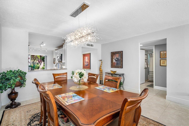 dining room with a textured ceiling, a chandelier, rail lighting, light tile patterned flooring, and sink