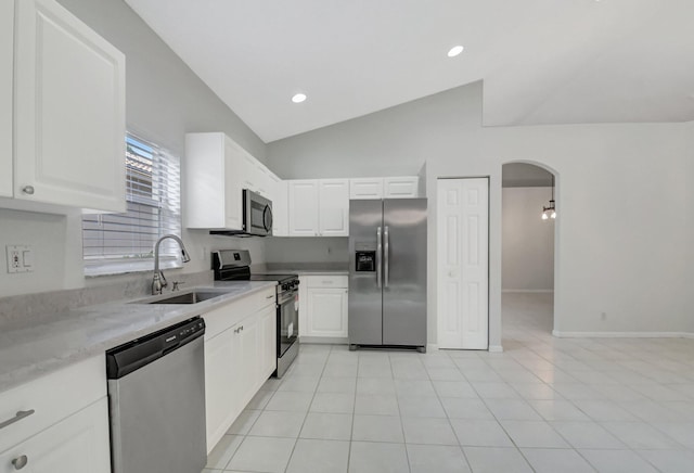 kitchen with appliances with stainless steel finishes, sink, white cabinets, lofted ceiling, and light tile patterned flooring