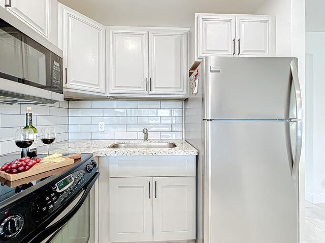 kitchen featuring appliances with stainless steel finishes, light stone countertops, white cabinetry, and sink