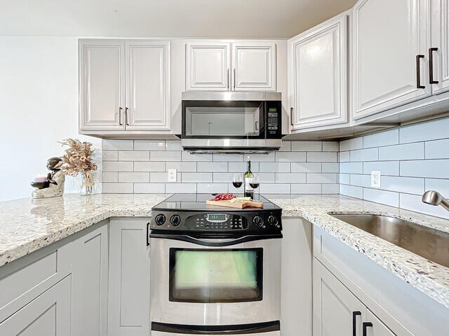 kitchen with white cabinets, sink, backsplash, appliances with stainless steel finishes, and light stone countertops