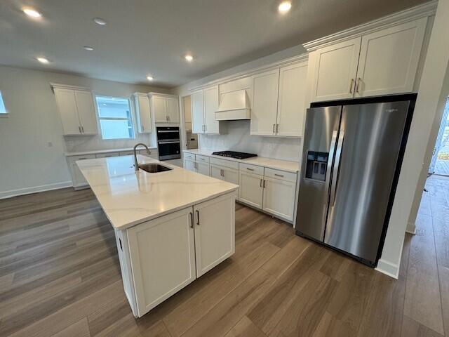 kitchen with white cabinetry, stainless steel refrigerator with ice dispenser, a kitchen island with sink, and custom exhaust hood