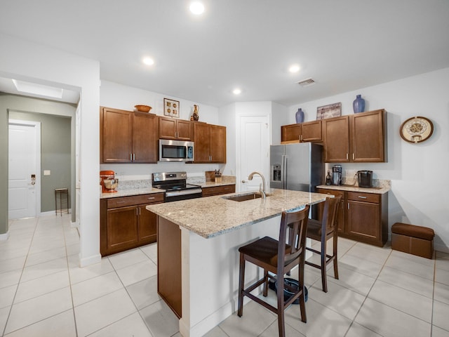 kitchen featuring light stone countertops, sink, a breakfast bar area, a kitchen island with sink, and appliances with stainless steel finishes