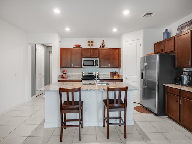 kitchen featuring appliances with stainless steel finishes, light stone counters, a kitchen island with sink, sink, and a breakfast bar area