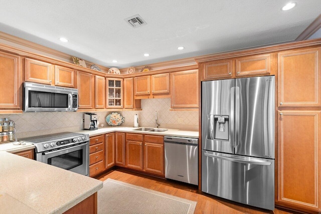 kitchen featuring appliances with stainless steel finishes, sink, light wood-type flooring, and decorative backsplash