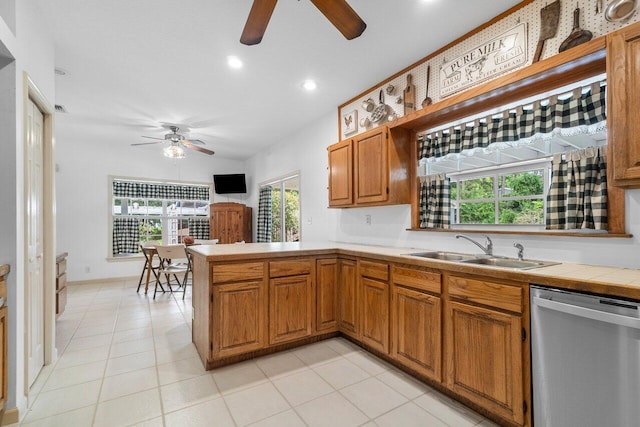 kitchen with light tile patterned flooring, sink, tile counters, dishwasher, and kitchen peninsula