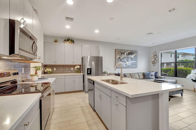 kitchen with an island with sink, stainless steel appliances, tasteful backsplash, white cabinets, and sink