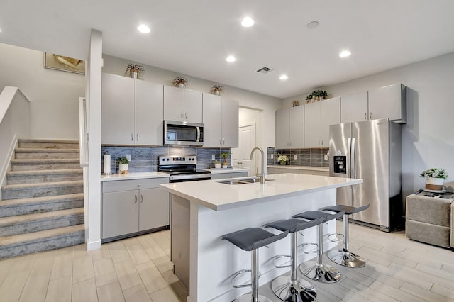 kitchen featuring a kitchen breakfast bar, a center island with sink, sink, decorative backsplash, and appliances with stainless steel finishes