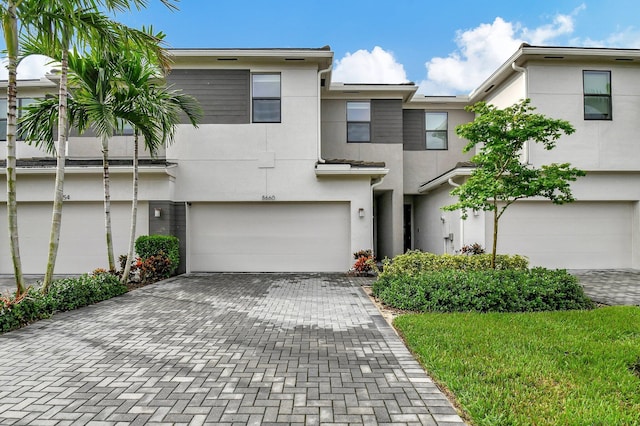 townhome / multi-family property with decorative driveway, an attached garage, and stucco siding