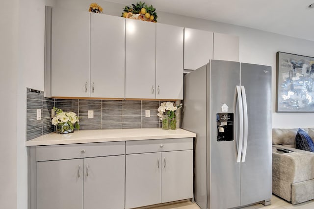 kitchen with light countertops, stainless steel fridge with ice dispenser, and tasteful backsplash