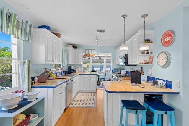 kitchen featuring light wood-type flooring, sink, hanging light fixtures, white cabinetry, and a kitchen bar