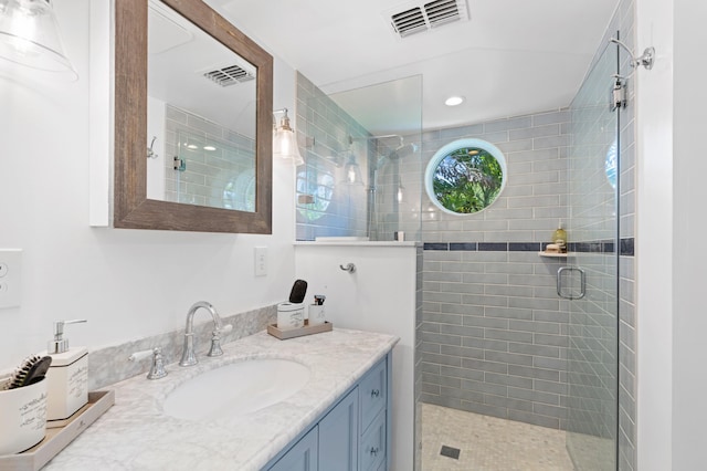 bathroom with visible vents, a tile shower, and vanity