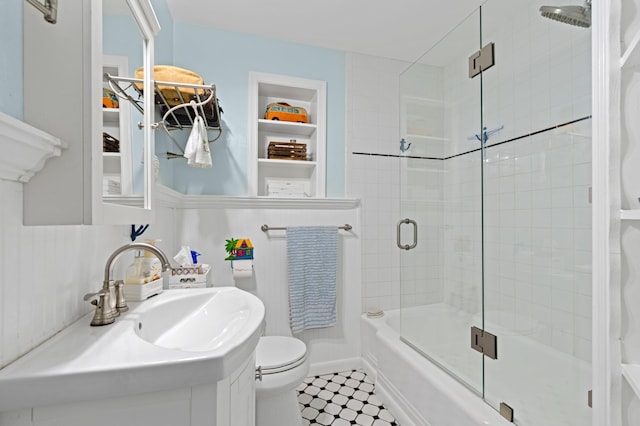 full bathroom with built in shelves, vanity, toilet, and bath / shower combo with glass door