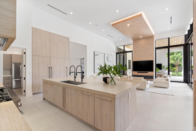 kitchen with stainless steel fridge, stove, light brown cabinets, sink, and a kitchen island with sink