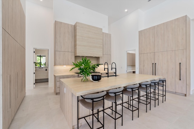 kitchen featuring a towering ceiling, light tile patterned floors, light brown cabinets, sink, and a kitchen island with sink