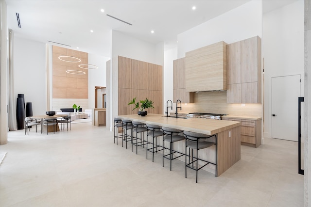 kitchen with tasteful backsplash, a kitchen breakfast bar, light brown cabinetry, light tile patterned floors, and an island with sink