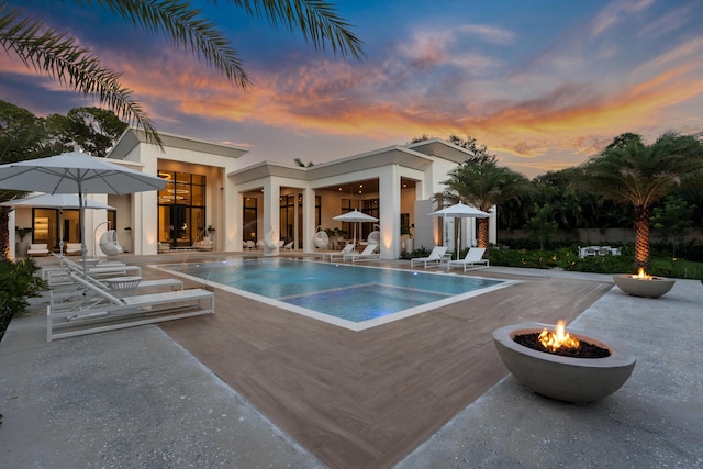 pool at dusk featuring a fire pit and a patio area