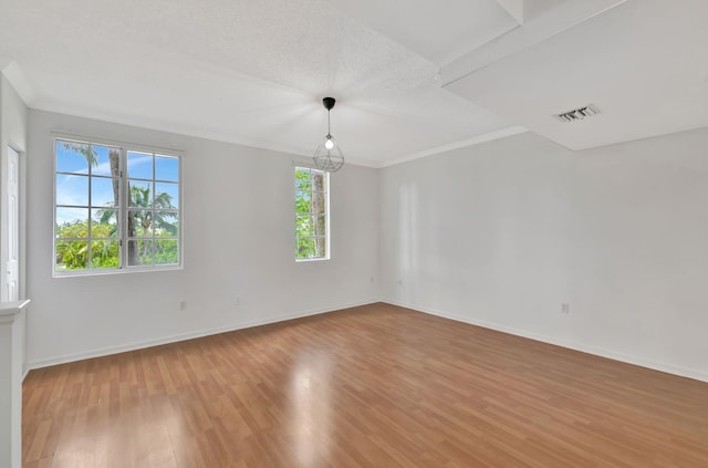empty room featuring light wood-style floors, baseboards, crown molding, and visible vents