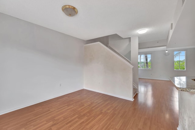 unfurnished living room featuring stairway, baseboards, a textured ceiling, and light wood-style flooring