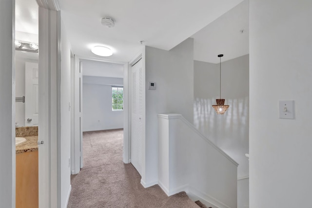 hall with baseboards, carpet, and an upstairs landing