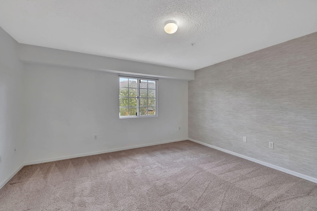 carpeted spare room featuring baseboards and a textured ceiling