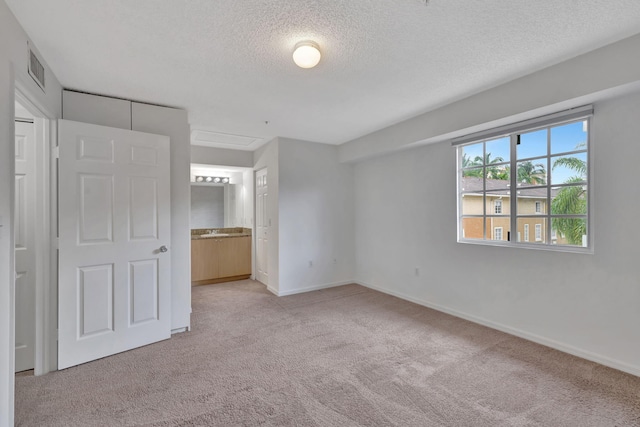 unfurnished bedroom with a textured ceiling, visible vents, baseboards, ensuite bathroom, and light carpet