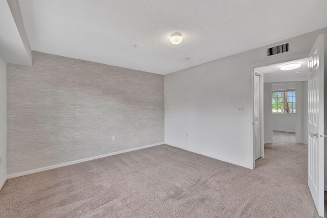 carpeted spare room with baseboards, a textured ceiling, and visible vents