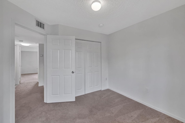 unfurnished bedroom featuring carpet flooring, a textured ceiling, visible vents, and a closet