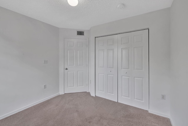 unfurnished bedroom featuring a textured ceiling, visible vents, baseboards, a closet, and carpet flooring